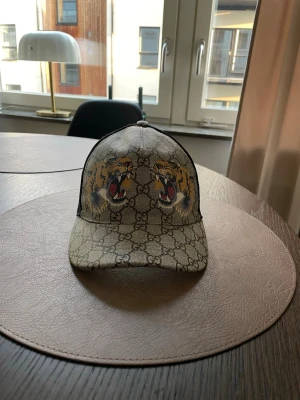 Gucci keps med tigertryck - Snygg och stilig Gucci keps i storlek S i fantastiskt skick. Säljes då jag inte använder den längre. Kepsen är självklart äkta och köptes av Kaspersheat för 2299kr så det är ett riktigt kap till den lyckliga köparen av kepsen. Kan frakta samt mötas upp i Västerås vid försäljning