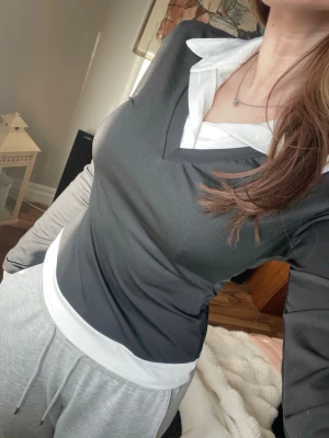 Svart långärmad topp med vit krage - Snygg svart långärmad topp med vit skjortkrage och v-ringning. Toppen har en figurnära passform och är perfekt för en trendig och stilren look. Materialet känns mjukt och stretchigt, vilket gör den bekväm att bära hela dagen.