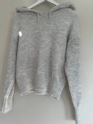 Ljusgrå stickad hoodie - Säljer denna stickade gråa hoddien från Gina Young i storlek 170. Tröjan har ribbade ärmar samt ribbad kant där nere. Använd ett fåtal gånger men ingenting som syns! 