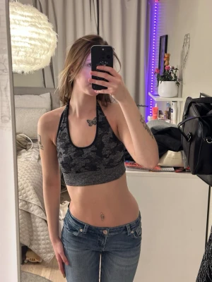 Grå camo träningstopp  - Säljer en grå träningstopp med camo-mönster och halterneck-design. Materialet är stretchigt och bekvämt, perfekt för att skapa en cool och sportig look. Bodyn har en djup urringning fram och är öppen i ryggen. Köpare står för frakt 😊