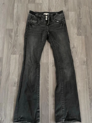 Svarta low waist bootcut jeans från Gina i tall - Snygga svarta bootcut jeans från Gina med två knappar i midjan och klassiska fickor fram och bak. Jeansen har en lätt tvättad look och markerade sömmar som ger en cool vibe. Perfekta för dig som gillar en lite vidare passform nertill. De är i tall.