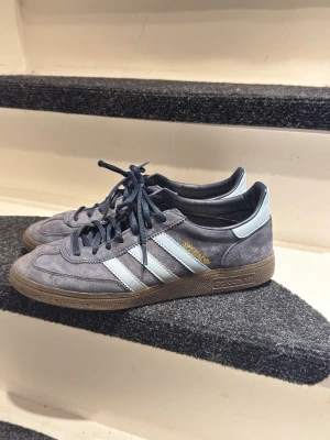 Adidas Spezial Navy  - Säljer ett par sparsamt använda Adidas Spezial i blå mocka med klassiska ljusblåa ränder på sidorna. Skorna har mörkblå snören och detaljer i ljusblått på hälen. Perfekta för dig som gillar retrostil och streetwear.