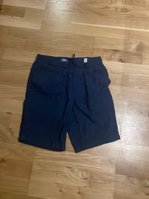Mörkblå shorts från Jack & Jones - Snygga mörkblå shorts från Jack & Jones med avslappnad passform och resår i midjan. Tillverkade i ett lätt tyg som passar perfekt för varma dagar. Klassisk design med fickor på sidorna och enkel look som funkar till det mesta.