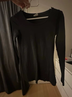 Svart långärmad topp - En enkel och stilren svart långärmad topp med rund halsringning. Perfekt att matcha med jeans eller kjol för en clean look. Materialet känns mjukt och stretchigt, vilket gör den bekväm att bära hela dagen.