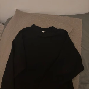 Svart stickad tröja från Nelly - Säljer en svart stickad tröja från Nelly med rund halsringning och ribbade detaljer vid halsen. Perfekt att matcha med jeans eller kjol för en stilren look