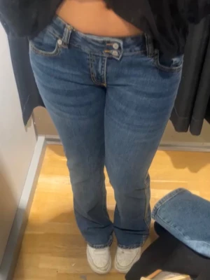 Blå bootcut jeans med låg midja - Säljer ett par klassiska blå bootcut jeans med låg midja och fem fickor. Jeansen har en snygg tvätt och subtila slitningar för en cool look. Perfekta till sneakers eller boots och passar dig som gillar en avslappnad men trendig stil. Stl är 38, men jag tycker de är mer i stl 40