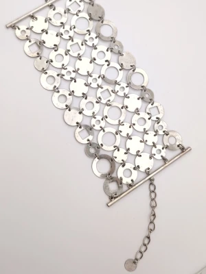 Brett silverfärgat armband i metall - Stilrent och brett armband i silverfärgad metall med geometriska former som cirklar och fyrkanter. Armbandet har en kedja för justerbar storlek och en unik, modern design som sticker ut. Perfekt för dig som gillar statement-smycken och vill ha något annorlunda. Patina men går att putsa bort om man vill