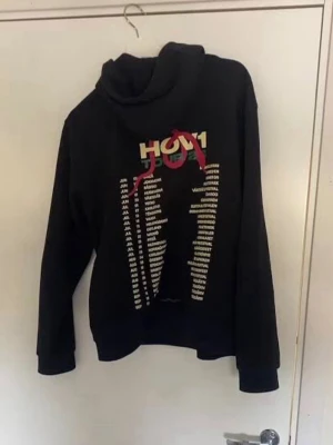 Svart hoodie med tryck från Hov1 - Säljer en svart hoodie från Hov1 med stort färgglatt tryck på bröstet och turnédatum i vitt. Såldes endast på deras turnering 23. Använd väldigt få gånger och ser ut som helt ny! Kom privat för fler bilder.
