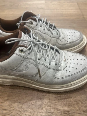 Nike beige sneakers- Air Force - Säljer ett par beige Nike sneakers i läder med klassisk swoosh på sidan och perforerade detaljer på tån. Skorna har bruna detaljer på insidan och beige snören med metalländar. Sulan är vit med en beige ton. Perfekta för en avslappnad streetwear-look.