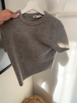 Grå stickad tröja från Zara - Mysig grå stickad tröja från Zara med rund halsringning och ribbade muddar. Tröjan har en enkel, klassisk design och är tillverkad i ett mjukt material som passar perfekt till kyligare dagar. Storlek xs