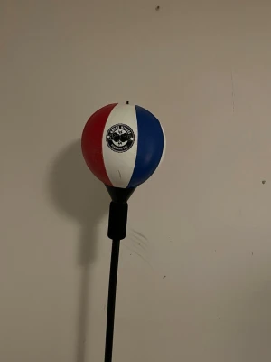 Boxningsboll på stång röd/blå/vit - Säljer en boxningsboll på stång från kance hinage. Bollen har färgerna röd, vit och blå och är monterad på en svart justerbar stång med stabil fot. Perfekt för träning av reflexer och snabbhet inom boxning eller kampsport.