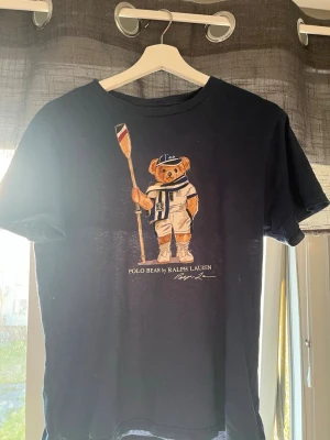 Marinblå Polo Bear t-shirt Ralph Lauren - Snygg marinblå t-shirt från Ralph Lauren med den ikoniska Polo Bear-trycket framtill. T-shirten har rund hals den e storlek L i barn storlek men skulle säga s 