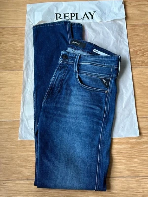 Mörkblå Replay jeans med smal passform - Snygga mörkblå jeans från Replay med smal passform och klassisk femficksdesign. Jeansen har subtila slitningar framtill och är tillverkade i stretchigt denim för extra komfort. Perfekta för en trendig och avslappnad stil.