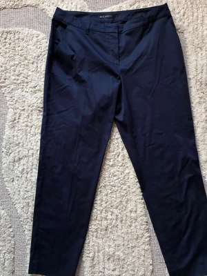 Mörkblå kostymbyxor Betty Barclay - Snygga mörkblå kostymbyxor från Betty Barclay med raka ben och diskreta fickor fram. Byxorna har klassisk dragkedja och knappstängning. Materialet är slätt och ger en stilren look, perfekt till en dressad outfit.