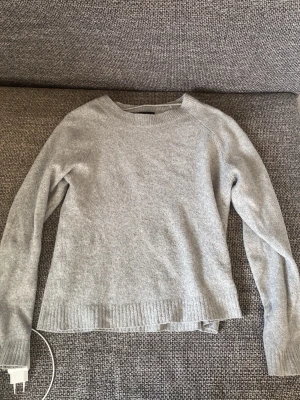 Ljusgrå stickad tröja - En enkel och stilren ljusgrå stickad tröja med rund halsringning och långa ärmar. Tröjan har ribbstickade muddar vid ärmslut och nederkant. Perfekt att matcha med jeans eller kjol för en avslappnad look.