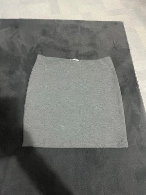 Grå kortkjol från Cubus - En enkel och stilren grå kortkjol från märket Cubus. Kjolen har en rak och tight passform som sitter snyggt på kroppen. Materialet är mjukt och stretchigt, vilket gör den bekväm att bära. Perfekt för dig som gillar minimalistisk och clean stil.