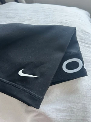 Nike Pro svarta träningsshorts - Svarta Nike Pro träningsshorta med vit Nike-logga på benet och bred resår i midjan med Nike Pro-tryck. Sitter tight och är gjorda i ett stretchigt och bekvämt syntetmaterial som andas, perfekt för sport och gym.