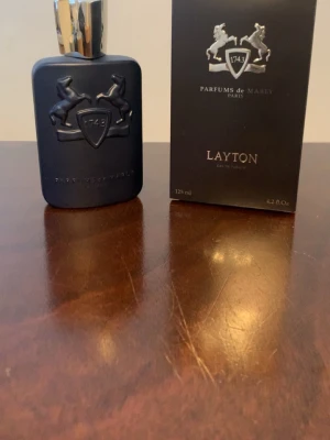 Parfums de Marly Layton EdP 125ml - Exklusiv parfym från Parfums de Marly, Layton Eau de Parfum i en matt mörkblå flaska med silverdetaljer och elegant logotyp med två hästar. Flaskan rymmer 125 ml och har en lyxig, modern design. Kommer med originalkartong i matchande färg.