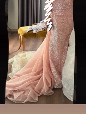 Glittrig rosa långklänning med släp - Säljer en fantastisk långklänning i rosa med glittriga paljetter och ett elegant släp i tyll. Klänningen har figurnära passform och är perfekt för speciella tillfällen. Supersnygg och unik design som verkligen sticker ut!