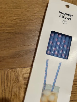 Blå sugrör med rosa blommor, 8-pack - Säljer ett paket med åtta blå sugrör dekorerade med små rosa blommor. Perfekta för drycker och smoothies. Sugrören är tillverkade i plast och kommer i en praktisk förpackning.