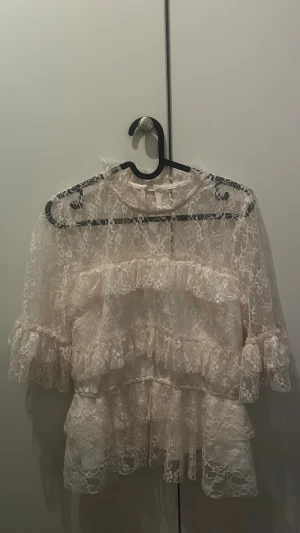 Vit spetsblus med volanger - Fin vit spetsblus med volanger och hög hals. Från bubbleroom, blusen har genombruten spets, trekvartsärm och knäppning i nacken.🤩 