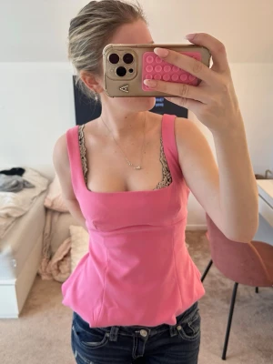 Rosa topp  - Säljer en snygg rosa korsett liknade topp med breda axelband och fyrkantig ringning. Toppens form är figurnära upptill och har en lätt utsvängd nederkant. Perfekt för dig som vill ha en trendig och feminin look.