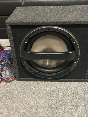 Phoenix Gold subwoofer med slutsteg - Säljer en kraftfull Phoenix Gold subwoofer i svart låda med inbyggt slutsteg. Lådan är klädd i grå filt och har anslutningskablar medföljer. Perfekt för dig som vill ha extra tryck i bilen eller hemma.