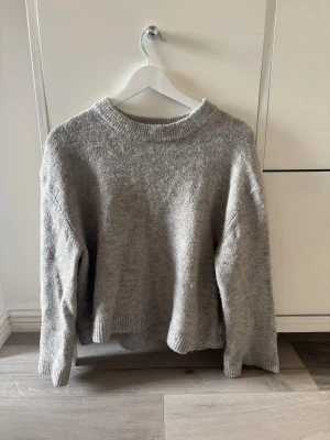 Grå stickad tröja från Gina Tricot - Mysig grå stickad tröja med avslappnad passform och rund halsringning. Tröjan har ribbade muddar vid ärmslut och nederkant samt en något boxig siluett. Perfekt för lager på lager och enkel att matcha med olika stilar. Från Ginatricot💕