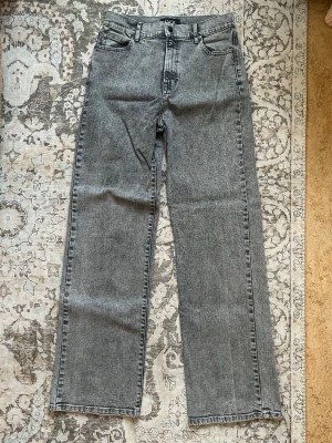 Grå raka jeans från IVY - Snygga grå raka jeans från IVY med klassisk femficksdesign och hög midja. Jeansen har en tvättad look och raka ben, perfekt för en avslappnad stil. Materialet är kraftig denim i bomull. Diskret IVY-brodyr på bakfickan.