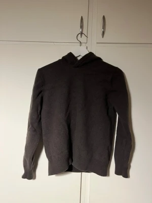 Mörkbrun stickad hoodie - Mysig mörkbrun stickad hoodie med huva och långa ärmar. Tröjan har en enkel och stilren design utan tryck eller detaljer, perfekt för en avslappnad look. Materialet känns mjukt och passar bra till alla.