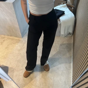 Svarta raka kostymbyxor från madlady  - Snygga svarta kostymbyxor med rak passform och hög midja. Byxorna har klassiska pressveck och diskreta fickor i sidorna. Perfekta för en clean och stilren look. Materialet ser ut att vara en mjuk och följsam mix, troligen polyester eller viskos. Insydda i midjan