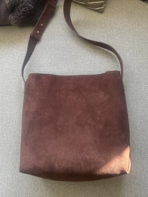 Brun axelväska  - Snygg brun axelväska med justerbart axelband från Kappahl. Väskan har en enkel, fyrkantig form och stängs upptill.🤎