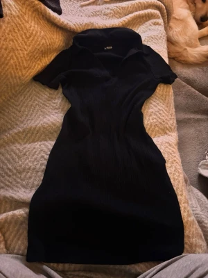 Svart ribbad kortklänning med krage - Svart ribbad kortklänning med krage och v-ringning. Klänningen har korta ärmar och en figurnära passform som framhäver siluetten. Perfekt för dig som gillar en stilren och enkel look. Nypris 250kr💕💕