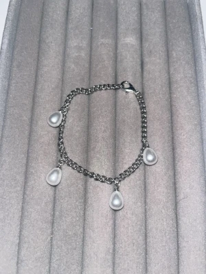 Silverfärgat armband med pärldroppar - Ett snyggt armband i silverfärgad metall med fyra droppformade vita pärlor som hänger från kedjan. Perfekt för dig som gillar stilrena och trendiga accessoarer med en touch av elegans.