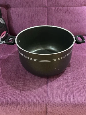 Stor svart gryta med handtag (IKKE INDEKTION) - En rejäl svart gryta i metall med två svarta plast- eller gummihandtag på sidorna. Grytan har rund form och två tunna silverfärgade linjer runt kanten. Perfekt för att laga större mängder mat eller soppor.