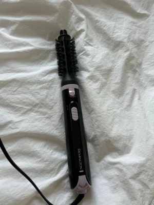 Värmeborste - Säljer en svart Värmeborste från Remington med borsthuvud och sladd. Borsten har lila detaljer och två reglage på handtaget för enkel användning. Perfekt för styling av håret och enkel att använda hemma.