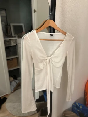 Vit långärmad topp med knyt - Trendig vit långärmad topp med v-ringning och snygg knytning framtill. Tunn och lätt i materialet, perfekt att styla med jeans eller kjol. Enkel men ändå chic design som passar till många olika looks.