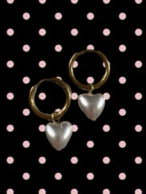 Guldiga hoops med hjärtformade pärlor - Snygga örhängen med guldiga hoops och hängande hjärtformade pärlor i vitt. Perfekta för att ge din look en söt och trendig touch. Passar dig som gillar stilrena accessoarer med en twist.