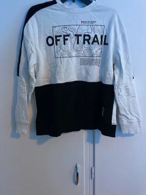 Vit och svart långärmad topp OFF TRAIL - Säljer en vit och svart långärmad topp med trycket 'OFF TRAIL' framtill och grafiskt mönster. Tröjan har rund halsringning och breda svarta partier nedtill och på ärmarna. Perfekt för en avslappnad streetwear-look.