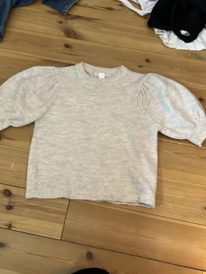 Beige stickad tröja med puffärm - Säljer en beige stickad tröja med puffärmar och ribbade muddar. Tröjan har en rak passform och rund halsringning. Perfekt för dig som gillar en enkel men trendig look. Materialet känns mjukt och bekvämt. Har använts så man kan se lite stickat som gått upp.