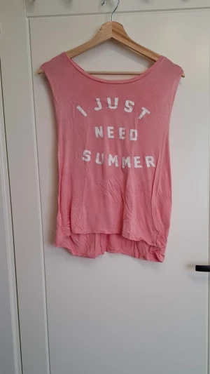 Rosa linnetopp från Young Romantics - Säljer en ljusrosa linnetopp från Young Romantics med trycket 'I JUST NEED SUMMER' i vitt på framsidan. Toppen är ärmlös med avslappnad passform och rund halsringning. Perfekt för varma dagar och enkel att styla med jeans eller shorts.