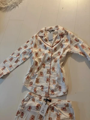 Pyjamas set - Söt och helt ny pyjamas från Bik Bok med gulligt kaninmönster. Set med långärmad skjorta med knappar framtill och matchande byxor med resår i midjan. Mjuk och skön kvalitet, perfekt för både mys hemma och sovkomfort.  Aldrig använd, lappar kvar. Storlek: S och XS Nypris: 660kr tillsammans