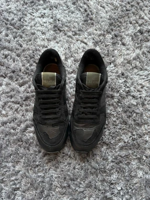 Svarta sneakers från Valentino - Snygga helsvarta sneakers från Valentino med coola detaljer i mocka och läder. Skorna har klassisk låg profil, svarta skosnören och diskret logga på plösen. Perfekta för dig som gillar stilrena och exklusiva sneakers. Skorna saknar sula!!