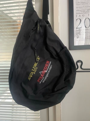 Svart ryggsäck Acqua Limone Pyramid - Cool svart ryggsäck från Acqua Limone med Pyramidens träningscenter-tryck i gult och rött. Ryggsäcken har en unik, trekantig form, justerbara remmar och dragkedjeficka framtill. Perfekt för gymmet eller skolan.