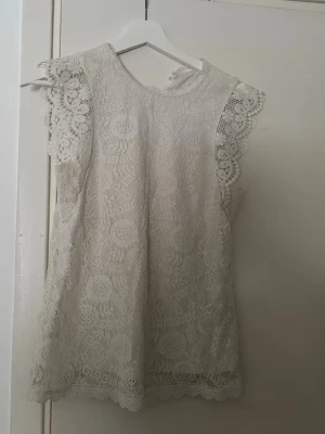 Vit spetsblus med volangärmar - Säljer en vit blus med vackert spetsmönster och volangdetaljer på ärmarna. Blusen är ärmlös och har en rund halsringning. Perfekt för dig som gillar romantiska och detaljerade toppar. Skriv för pris förslag elelr fler bilder❤️