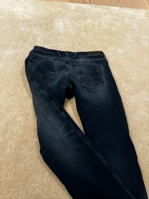Mörkblå jeans från Replay - Säljer ett par mörkblå jeans från Replay med klassisk femficksmodell. Jeansen har raka ben och detaljerade bakfickor med Replay-logga på linningen. Tillverkade i mjuk denim för skön passform.