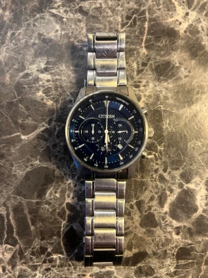 Citizen kronografklocka i stål - Snygg Citizen herrklocka med blå urtavla och flera subdials. Klockan har en robust länk i silverfärgat stål och tydliga markeringar. Perfekt för dig som gillar klassisk men sportig stil. Urtavlan har tachymeter och datumvisning.