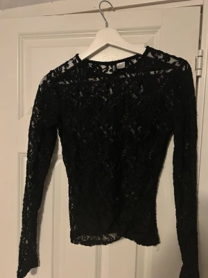 Svart spetsblus med lång ärm - Säljer en svart, transparent topp!. Toppen har lång ärm och är täckt av ett blommigt spetsmönster som ger en elegant och trendig look. 