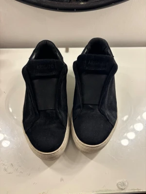 Svarta slip-on sneakers från Axel Arigato - Svarta Axel arigato skor, i bra skick. Säljs pga dålig ansvänding. Väldigt sköna i storlek 38💓💓