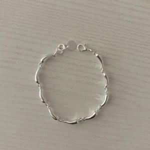 Paket pris  - Säljer två stilrena armband i silverfärg. Det ena har vågformade länkar och det andra är ett tunt armband med ett hjärta och en liten pärldetalj. Båda är perfekta för att addera en elegant touch till din outfit. Materialet